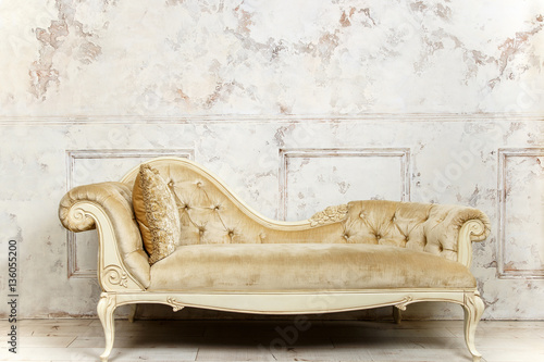 Luxurious golden sofa on a background of old white wall