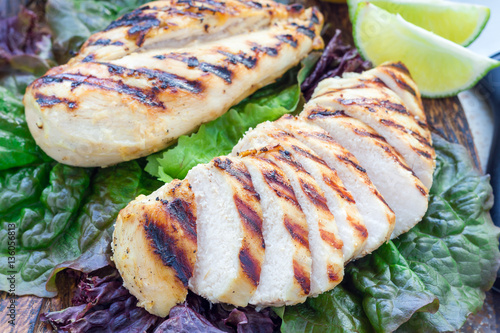 Grilled chicken breast in citrus marinade on salad leaves and wooden cutting board, horizontal