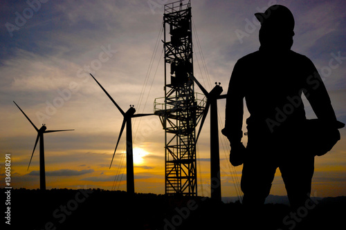  The silhouette of an engineer standing at a power station and wind turbine towers.