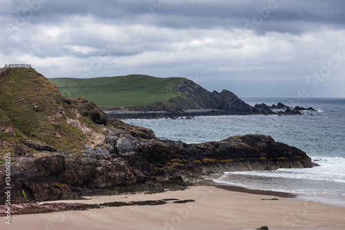 North Coast, Scotland - June 6, 2012: Cliffs descend on Durness Beach, a sandy patch looking north on a rough coast among rock cliffs and sprinkled pieces of rock.