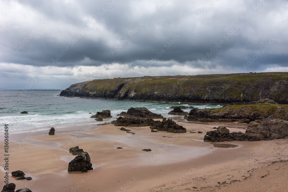 North Coast, Scotland - June 6, 2012: Cliffs descend on Durness Beach, a sandy patch looking north on a rough coast among rock cliffs and sprinkled pieces of rock. North Coast, Scotland - June 6, 2012: Cliffs descend on Durness Beach, a sandy patch looking north on a rough coast among rock cliffs and sprinkled pieces of rock.