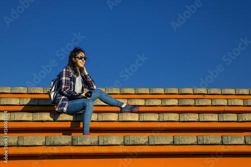 Young and stylish woman with camera sitting on the bech on sunny