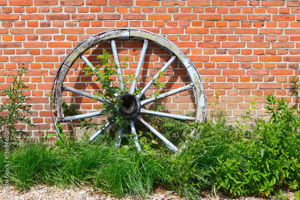 Big, old wagon wheel against the background of a wall from a red brick