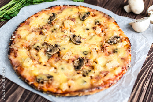Hawaiian pizza with meat, mushrooms and pineapple on a wooden background