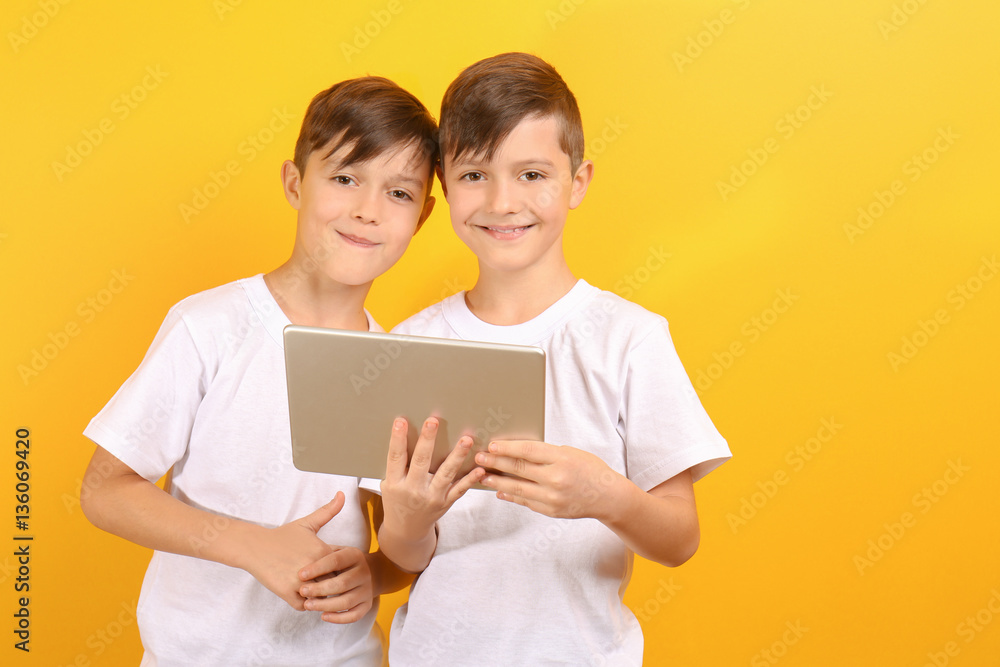 Twin brothers with tablet on yellow background Twin brothers with tablet on yellow background