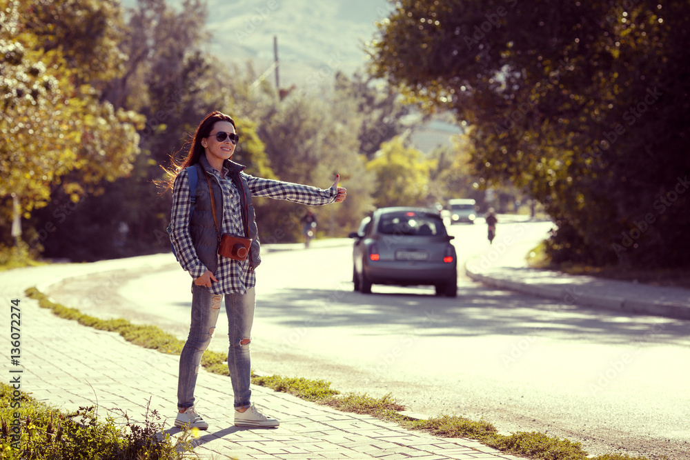 Fototapeta premium young woman hitch-hiking on a road at the fields