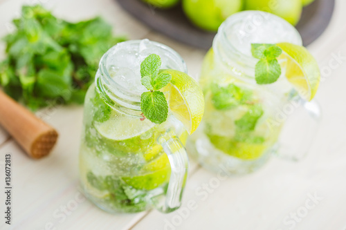 Two fresh mojitos cocktail in mason jar on wooden background. Mojitos with mint leaves, lime and ice. Drink making tools and ingredients for cocktail.