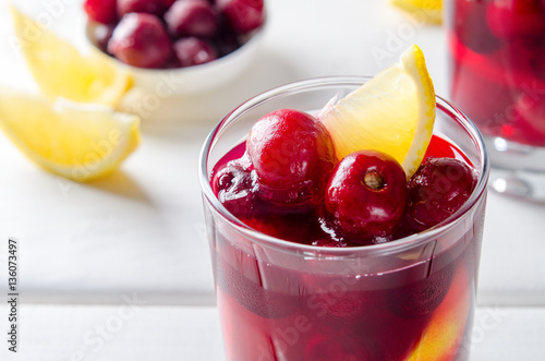 Cold drink with cherry and lemon in glasses, on white wooden background