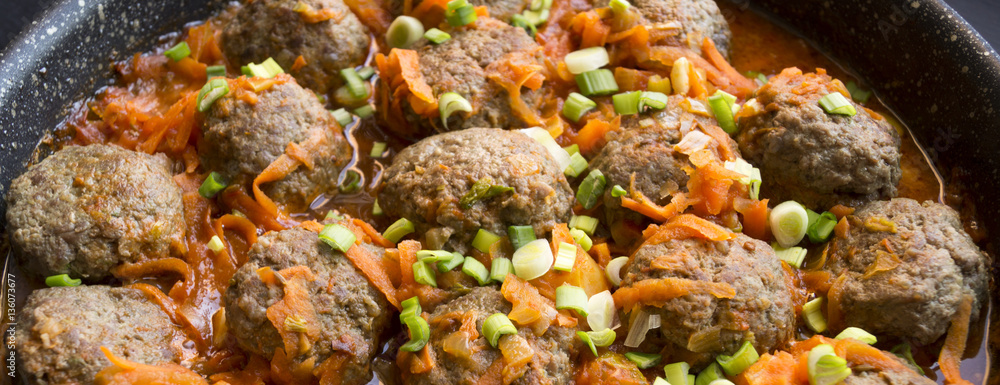 Meatballs in tomato sauce with green onions on a dark background