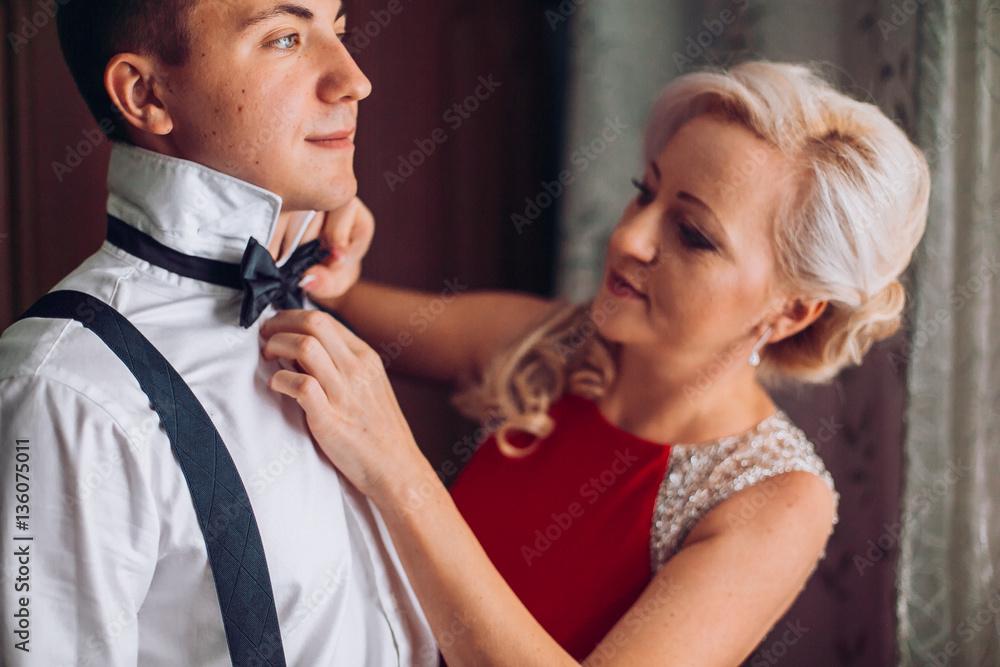 Mother is helping with a bow-tie to her son before wedding ceremony. Concept mother and son.