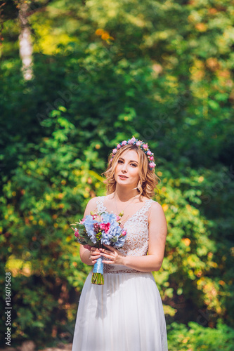 bride with flowers in hand outdoor. Blond woman circle wedding dress.