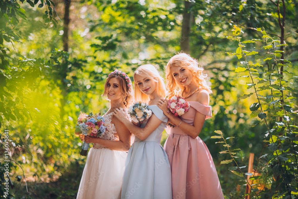 Amazing blond girls. Bride with bridesmaids with flowers hand in medow sunny pine forest.