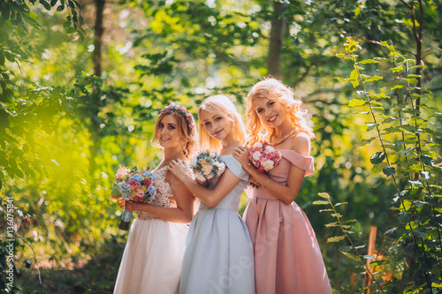 Obraz na płótnie Amazing blond girls. Bride with bridesmaids with flowers hand in medow sunny pine forest. w salonie