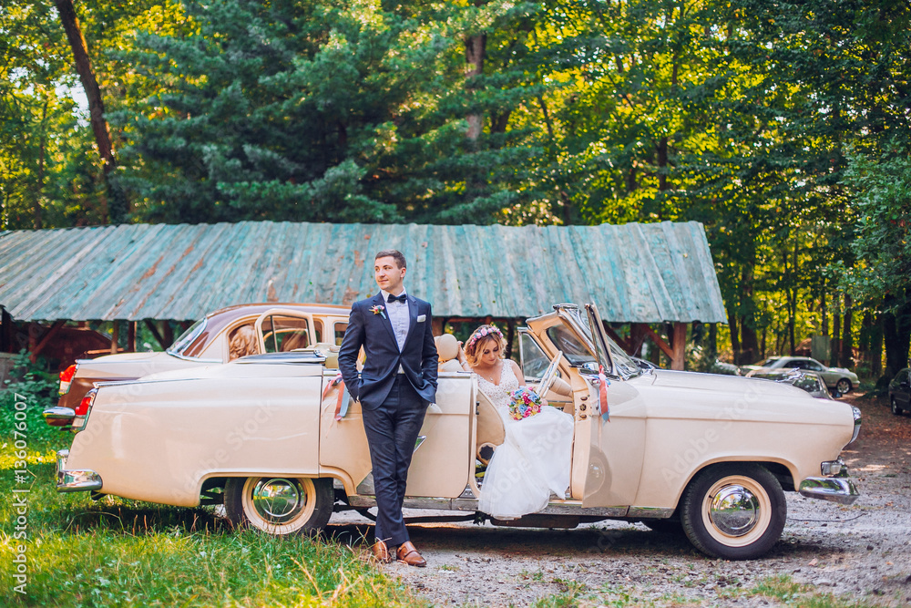 Stylish Loving wedding couple kissing and hugging on nature near retro car