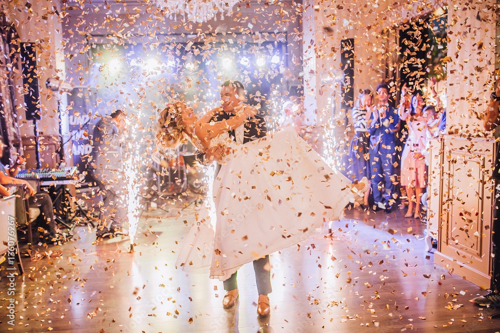 Bride and groom first dance at wedding reception with firewoks and confetti. Kissing and swing couple in love.
