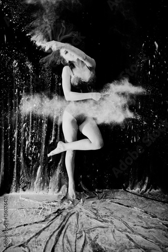 Girl dancer jumping and dancing in the white dust with flour on photo