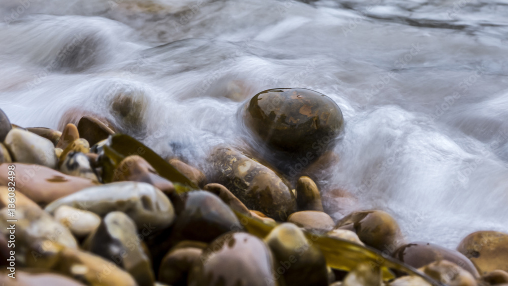 Obraz premium Close up of pebbles on the coast of the ocean with a wave coveri
