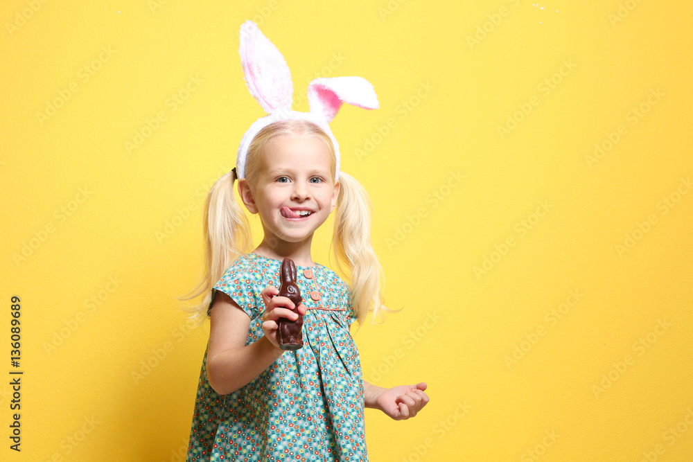 Cute little girl with bunny ears and chocolate rabbit on color background Cute little girl with bunny ears and chocolate rabbit on color background