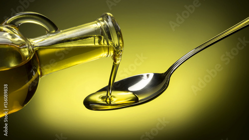 bottle pouring oil in a spoon on green background