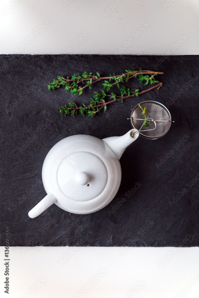 Teapot with strain and thyme on slate. Top view. Selective focus.