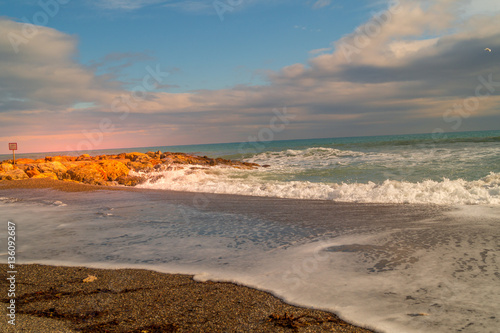 sea landscape. Beach with waves and rocks, sky with clouds and sun. Sunset on beach