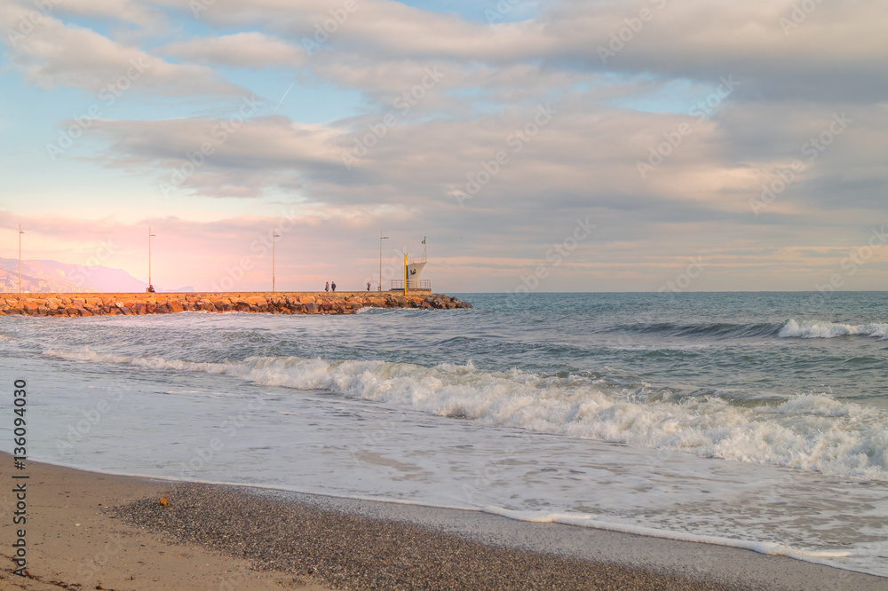 sea landscape. Beach with waves and rocks, sky with clouds and sun. Sunset on beach