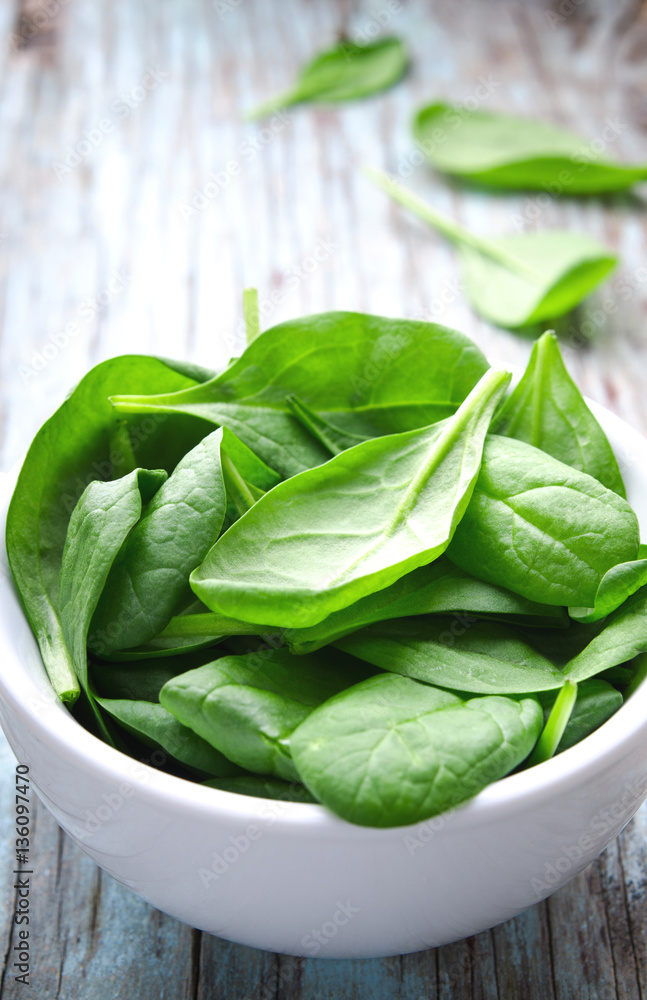 Fresh Baby spinach leaves in white bowl on blue wooden background. Top view with copy space, vertical. Healthy, Ecology concept Fresh Baby spinach leaves in white bowl on blue wooden background. Top view with copy space, vertical. Healthy, Ecology concept