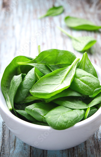 Fresh Baby spinach leaves in white bowl on blue wooden background. Top view with copy space, vertical. Healthy, Ecology concept