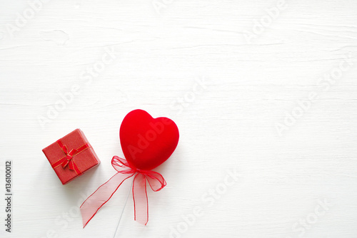 Red heart and gift red box with a bow on a wooden white background. Romantic card. Gift by St. Valentine's Day.