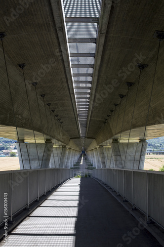 Pedestrianized road is beneath motorway, coupled concrete and steel.