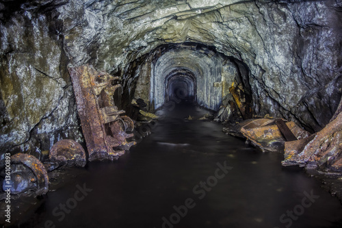 The tunnel of an old abandoned mine with rusty remnants of trolleys
