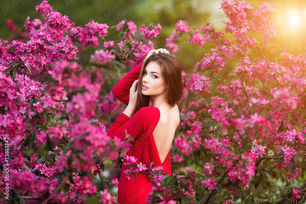 Spring touch. Happy beautiful young woman in red dress enjoy fresh pink flowers and sun light in blossom park at sunset. Spring touch. Happy beautiful young woman in red dress enjoy fresh pink flowers and sun light in blossom park at sunset.