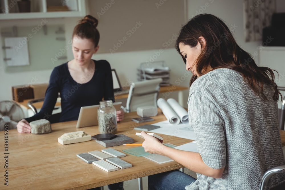 Business executive looking at stone slab while colleague using digital tablet in office Business executive looking at stone slab while colleague using digital tablet in office