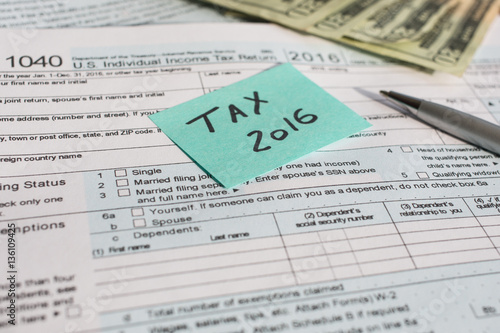 A shot of US Income Tax time 2016 written on a written on a bright sticker and tax form 1040 with pen and twenty dollars banknotes US 1040 tax form