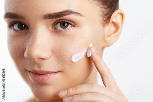 Attractive girl putting anti-aging cream on her face. Closeup Portrait Of Girl With Healthy Smooth Skin