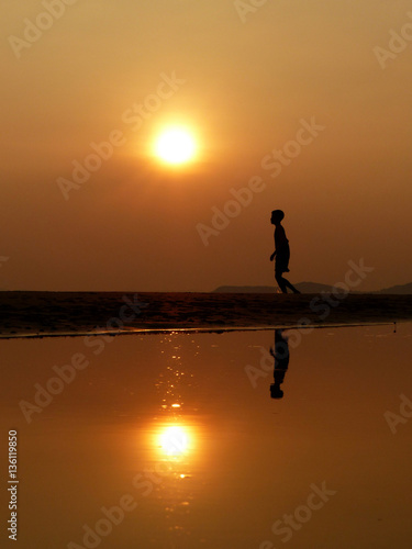 Silhouette boy walking on the beach at sunset