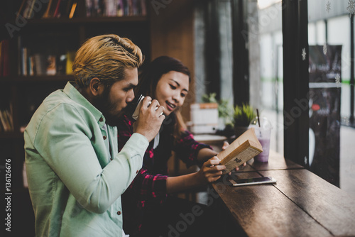Hipster couple on vacation sitting in indoors cafe reading book.