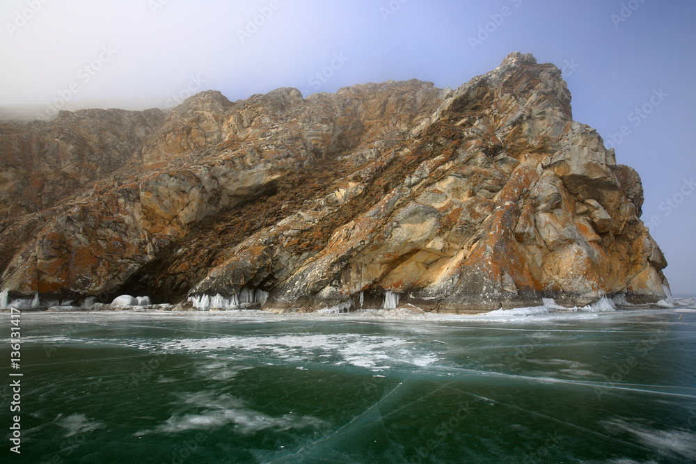 Rocky shore of lake Baikal in the fog in winter Rocky headland on the Western coast of lake Baikal sticks in ice-covered body of water, Fog hampers visibility Rocky shore of lake Baikal in the fog in winter Rocky headland on the Western coast of lake Baikal sticks in ice-covered body of water, Fog hampers visibility