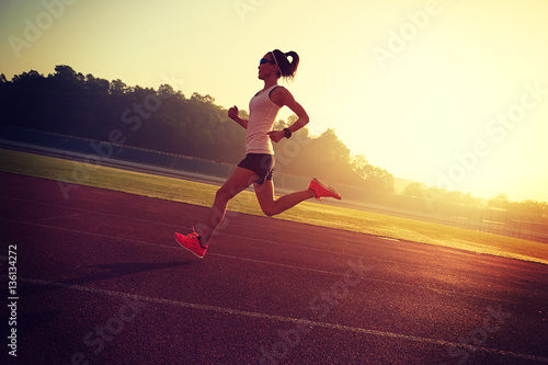 Young woman running during sunny morning on stadium track © lzf