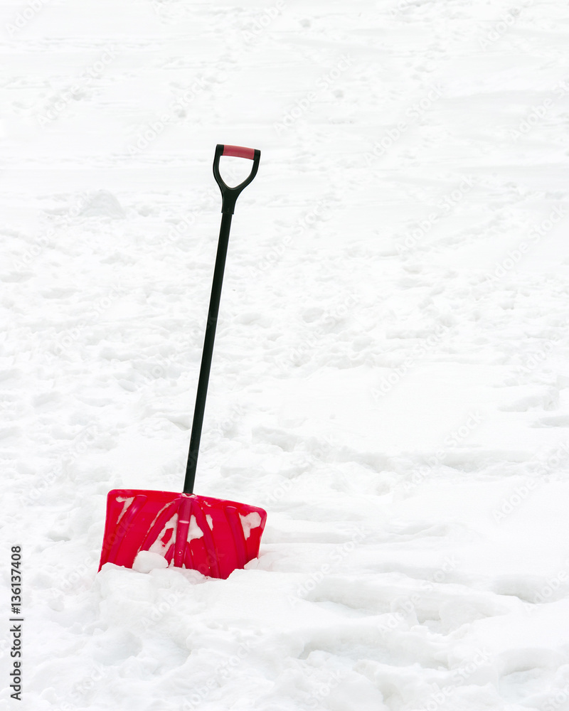 Fototapeta premium Red plastic shovel with black handle stuck in fluffy white snow.
