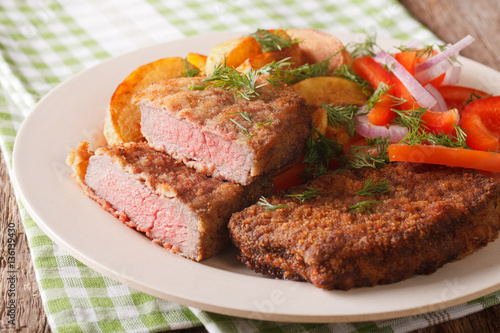 rump steak in breadcrumbs and fresh vegetables, baked potatoes close up. Horizontal