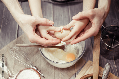 Little girl and her mother cook dough for home-made cupcakes. 