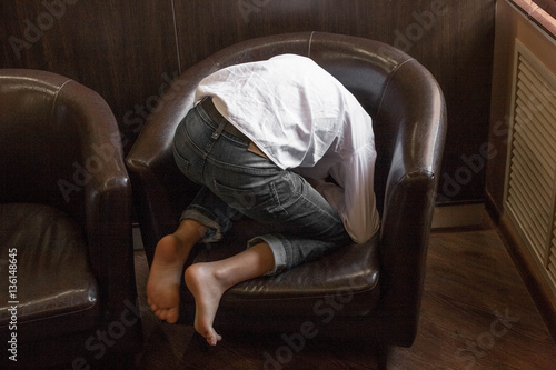 Boy in white shirt sitting in a chair. young boy imposingly placed in a leather couch. boy in shirt and jeans. Teenager relaxing in a cafe
 photo