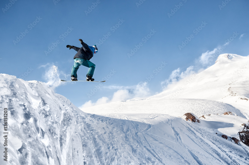 Stylish snowboarder with helmet and mask jumps from high snow slope Stylish snowboarder with helmet and mask jumps from high snow slope