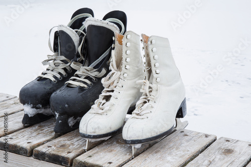 Old white and black skates on the wooden bench at ice area in winter day. Weekends activities outdoor in cold weather.