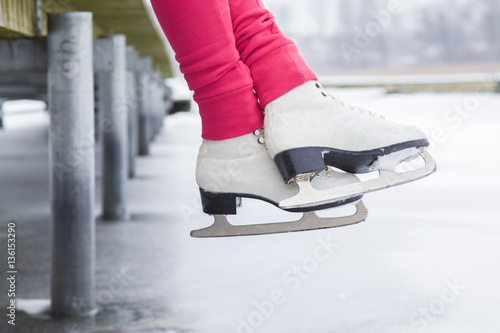 Woman sitting on the bridge on the lake with white skates in winter day. Weekends activities outdoor in cold weather.