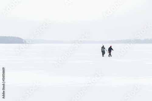 Two anglers going to fishing on the lake ice in winter day. Fisherman.