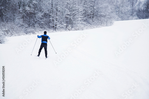 Skier  with skis on the snow track beside forest in the winter day. Country skiing.