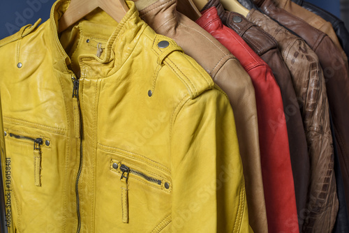 Many colored  leather jacket hanging on rack on blue background