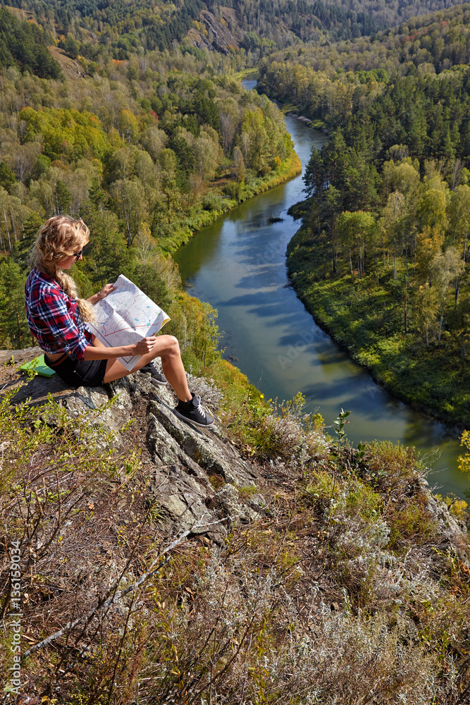 Young blonde woman tourist sitting on a cliff with map in hands Young blonde woman tourist sitting on a cliff with map in hands